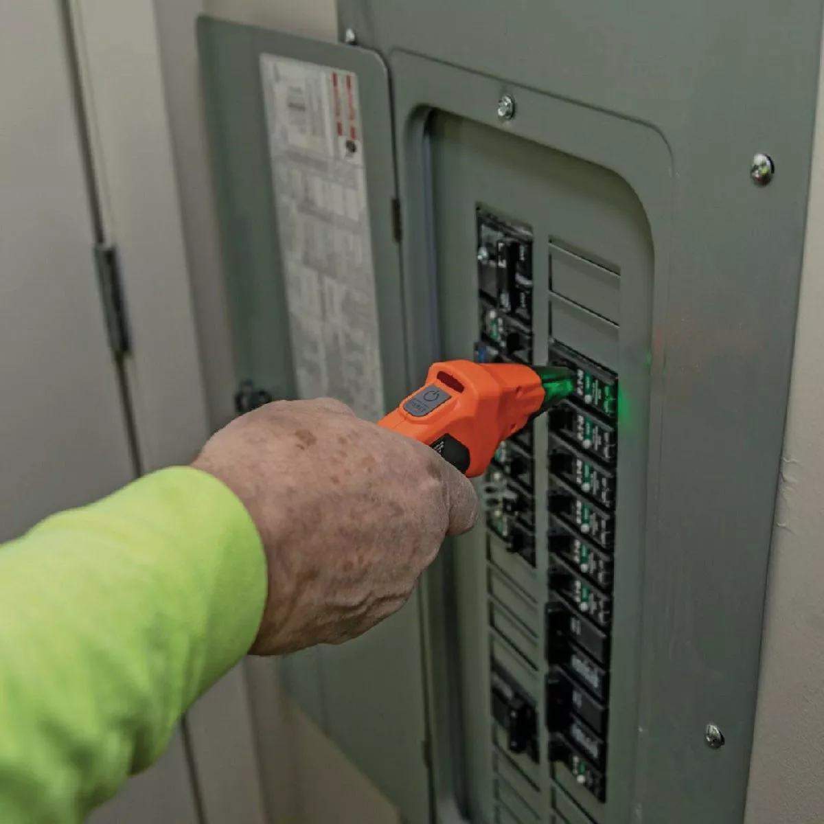 Hand using orange Klein circuit tester on electrical breaker panel for tools and home improvement jobs