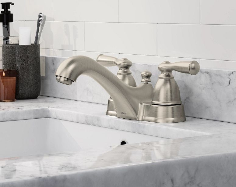 Moen stainless two-handle low arc faucet installed on a marble bathroom sink countertop with white tile backsplash