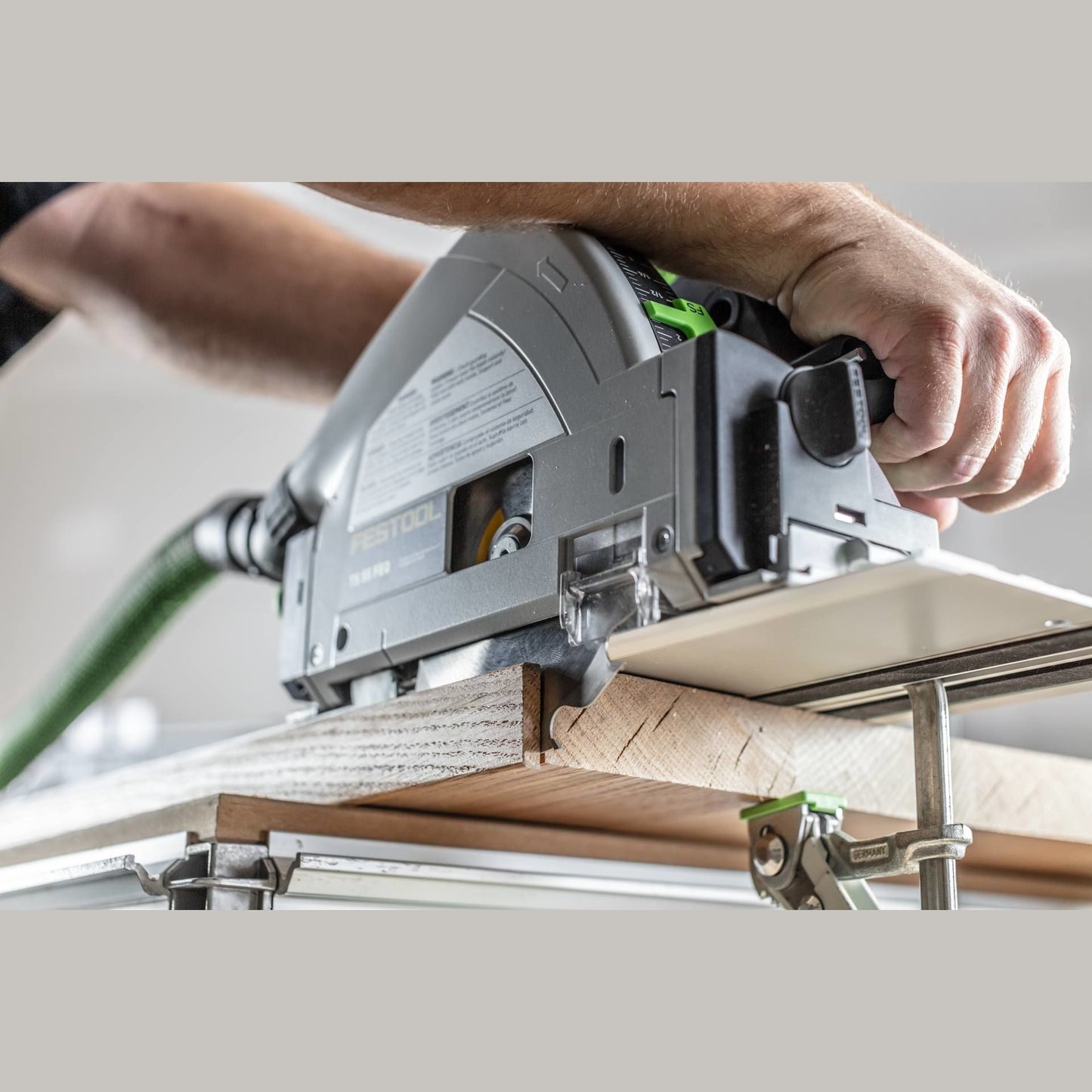 Hands operating a plunge-cut track saw on wood supported by clamps and a guide rail in a workshop setting