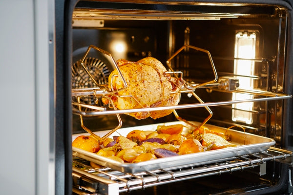 Professional stainless steel double wall oven with rotisserie cooking whole chicken and roasted vegetables inside
