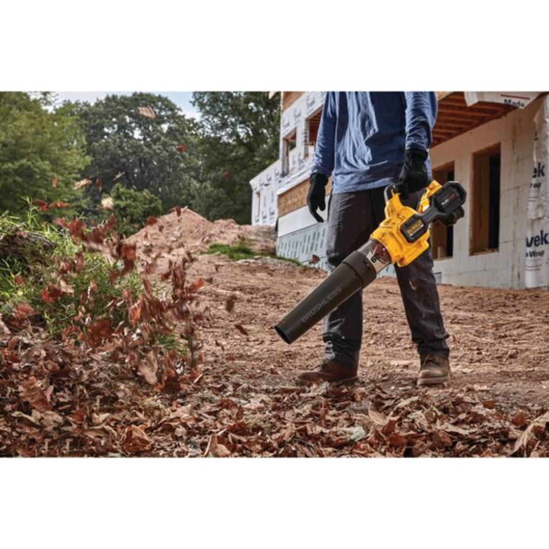 Cordless yellow handheld axial blower clearing dry leaves outdoors at a construction site for home improvement tasks