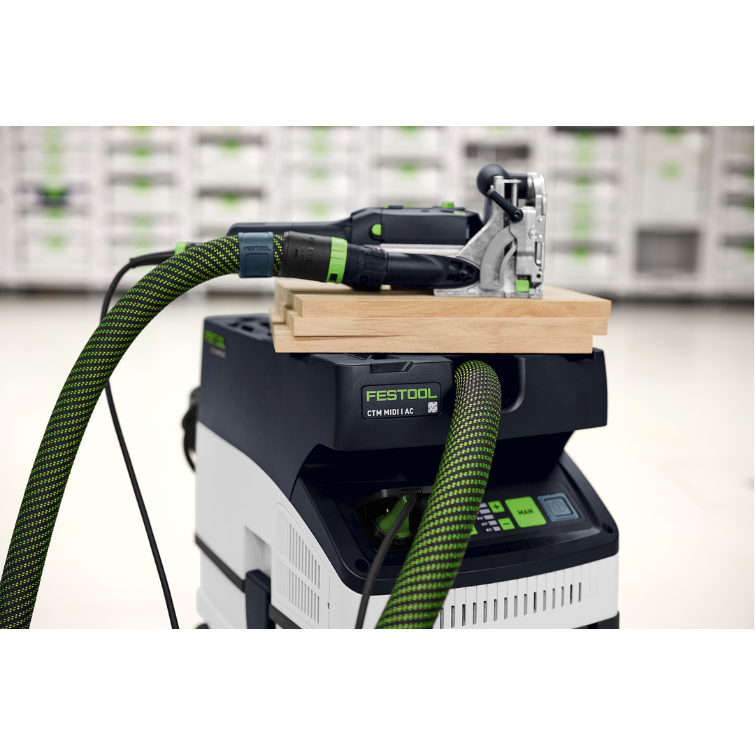 Festool woodworking joiner connected to a dust extractor with green hose, set up on a workbench with stacked light wood pieces, showcasing precision tools from the Woodworking Power Tools and Electric Power Tools collections.