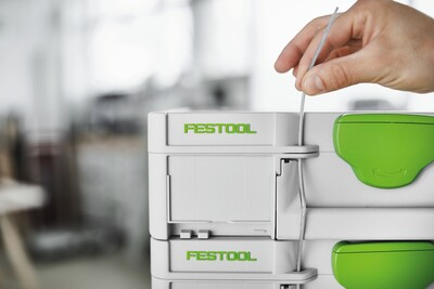 Hand adjusting latch on white and green Festool modular tool storage box for workshop organization
