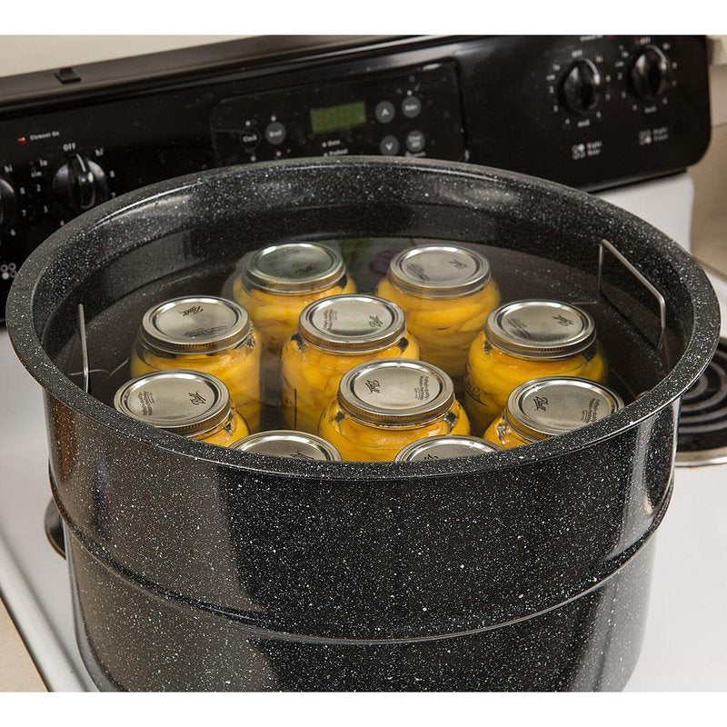 Black speckled covered preserving canner pot holding glass jars filled with yellow preserved food on stovetop burner