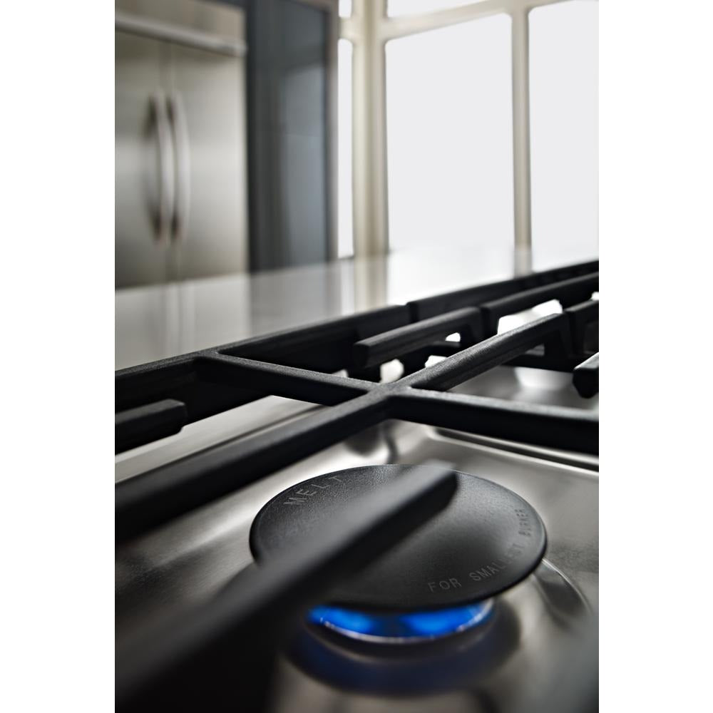 Close-up of stainless steel gas cooktop burner with blue flame in modern kitchen setting