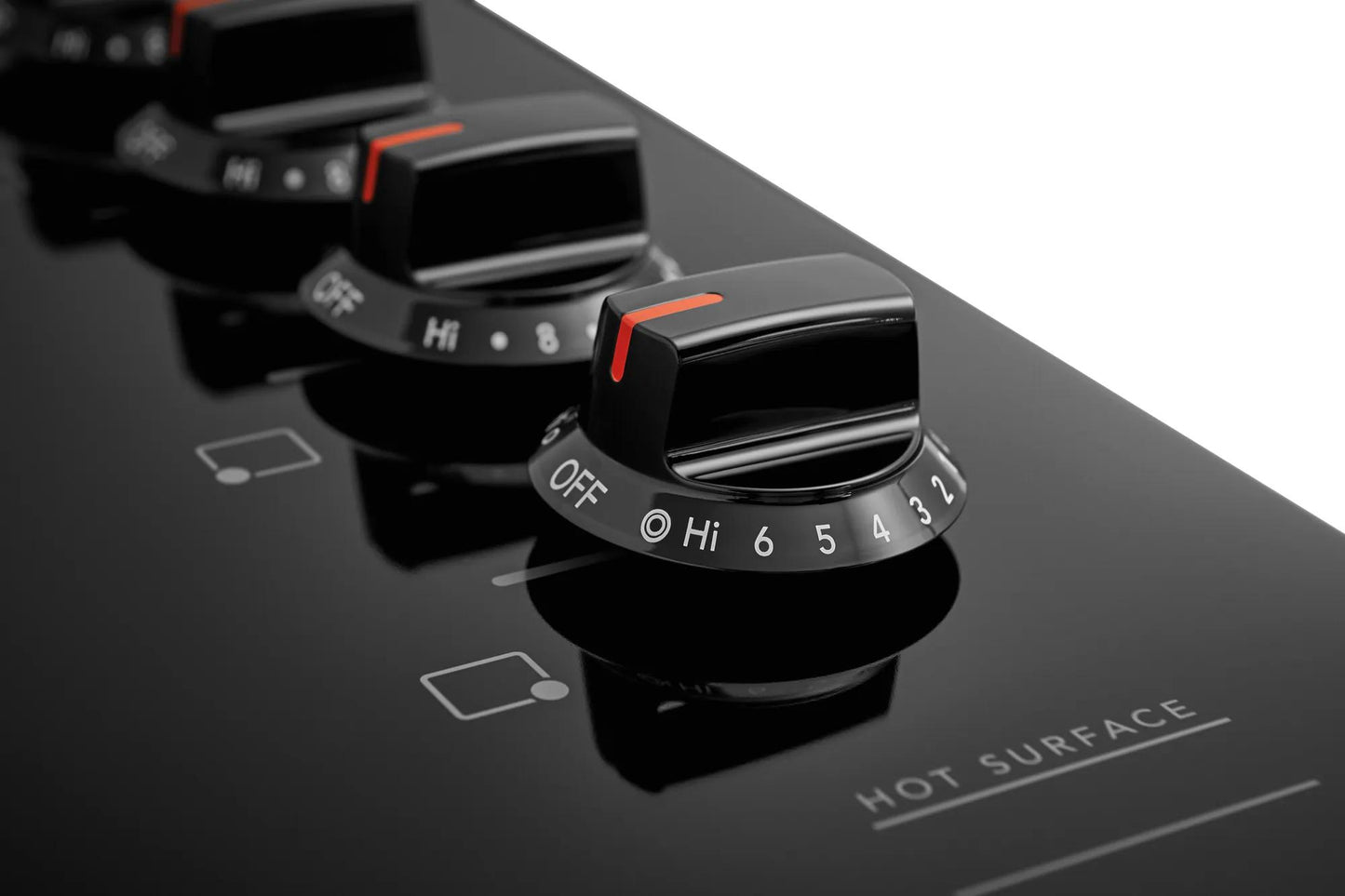 Close-up of black rotary control knobs with numbered heat settings on black frameless electric cooktop in appliances collection