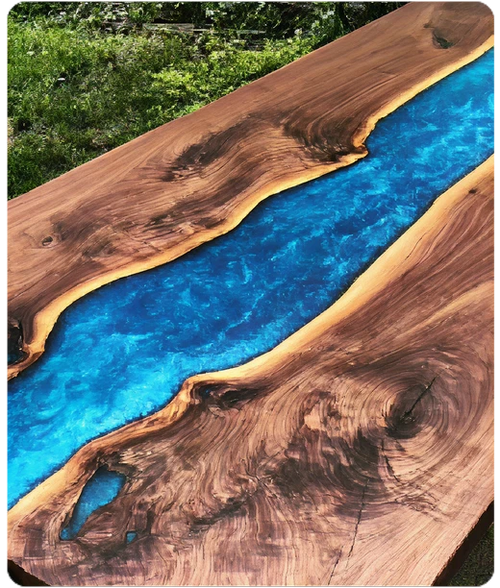 Wood surface table with natural live edge design featuring a vibrant blue resin river running through the center, set outdoors on grass.