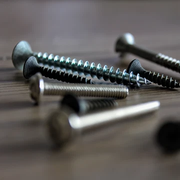 Assorted metal screws scattered on a wooden surface with shallow depth of field highlighting the threads on a central screw.