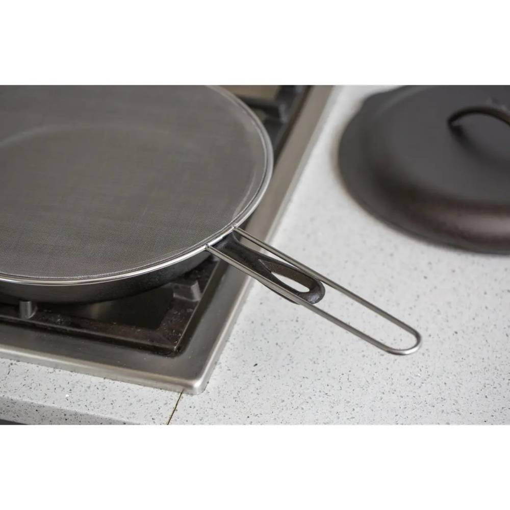 Round stainless steel mesh splatter screen with wire handle resting on gas stove in kitchenware collections