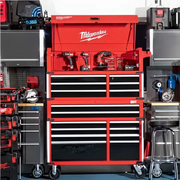 Red Milwaukee-branded metal tool chest with multiple black drawers, open top compartment displaying various cordless power tools, surrounded by additional storage units and equipment.
