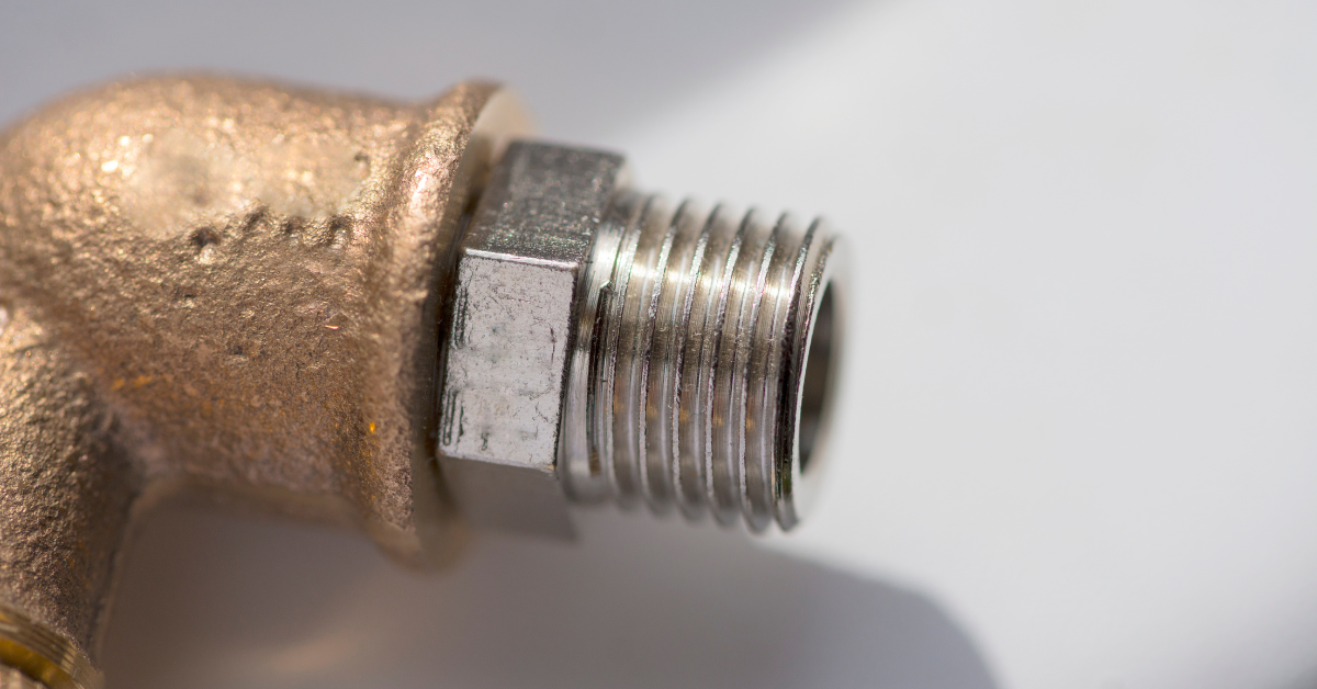 Close-up of a brass plumbing elbow fitting with a threaded steel pipe connector attached, shown against a plain white background.