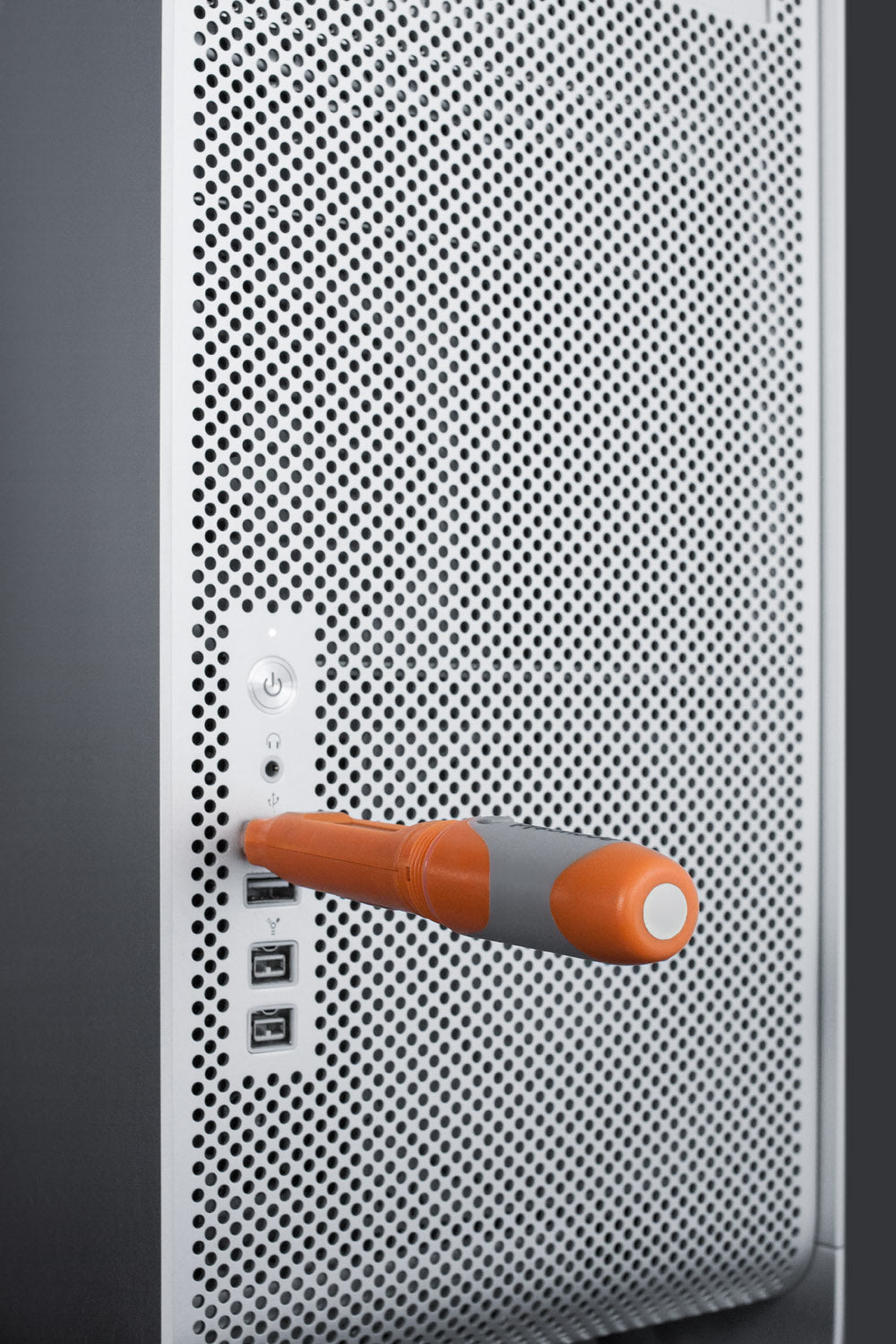 Orange and gray portable data logger inserted into a perforated metal surface with USB ports visible
