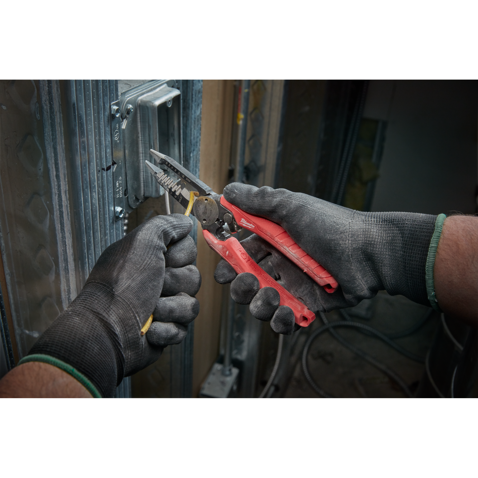 Hands in black gloves using red comfort grip pliers to strip yellow electrical wire for home improvement tasks