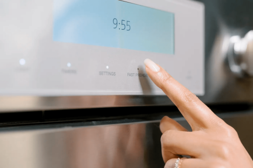 Close-up of finger pressing fast preheat button on stainless steel double wall oven control panel in appliance collection