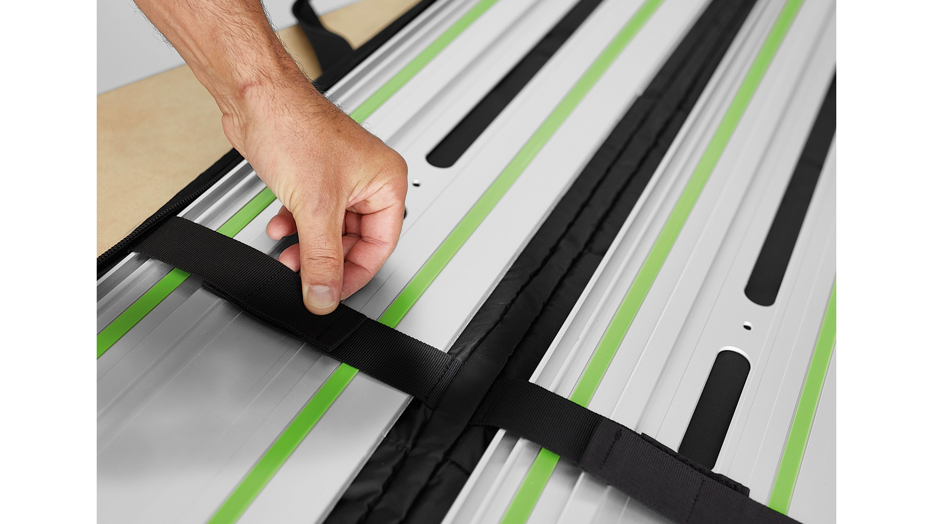 Hand securing black strap on aluminum Festool guide rails in woodworking tool accessories setup