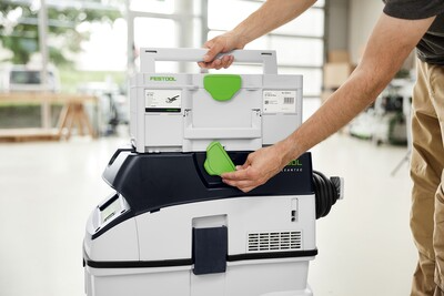 Person attaching white and green HEPA filter module onto Festool dust extractor for woodworking tools use