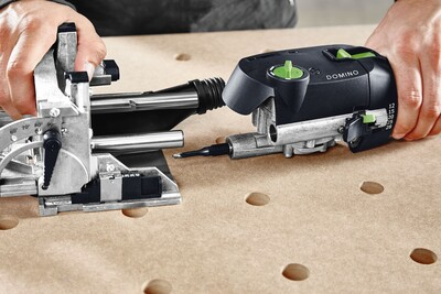 Hands operating a Festool Domino joinery tool on a perforated wooden board for woodworking power tools collection