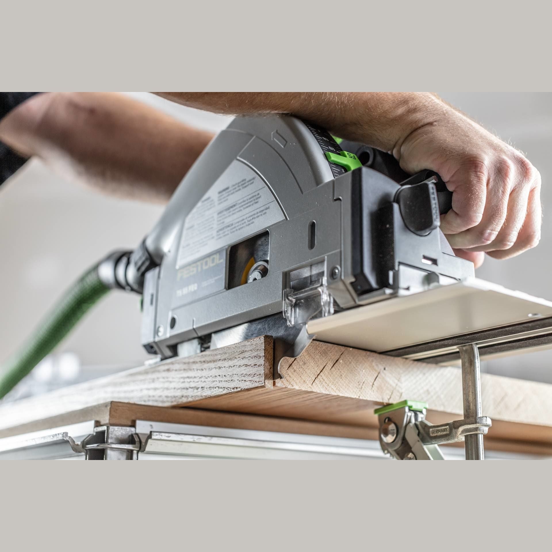 Hands operating a plunge-cut track saw on wood supported by clamps and a guide rail in a workshop setting