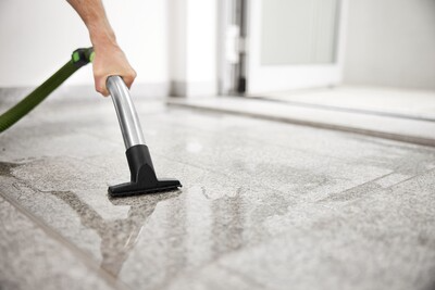 Person using a metal nozzle attached to a green hose for cleaning a tiled floor with a Festool dust extractor in a workshop setting