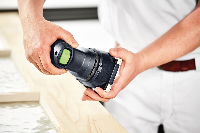 Hands holding a black Festool sander protector with green button over a wooden board for home improvement tasks