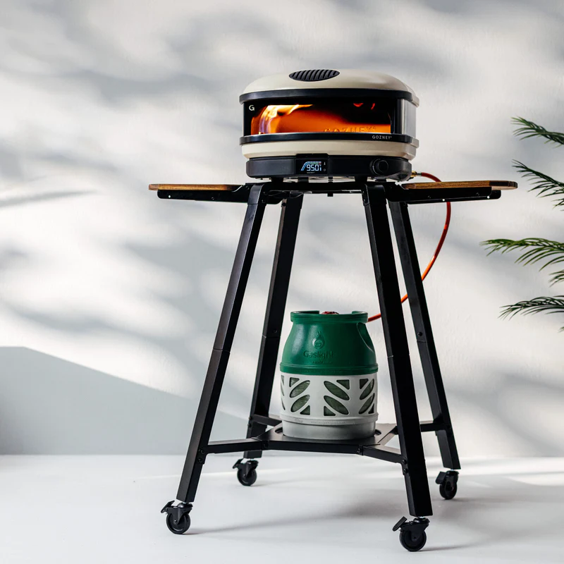 Metal stand with caster wheels and wooden side shelves holding an outdoor cooking oven and propane tank for grilling collections