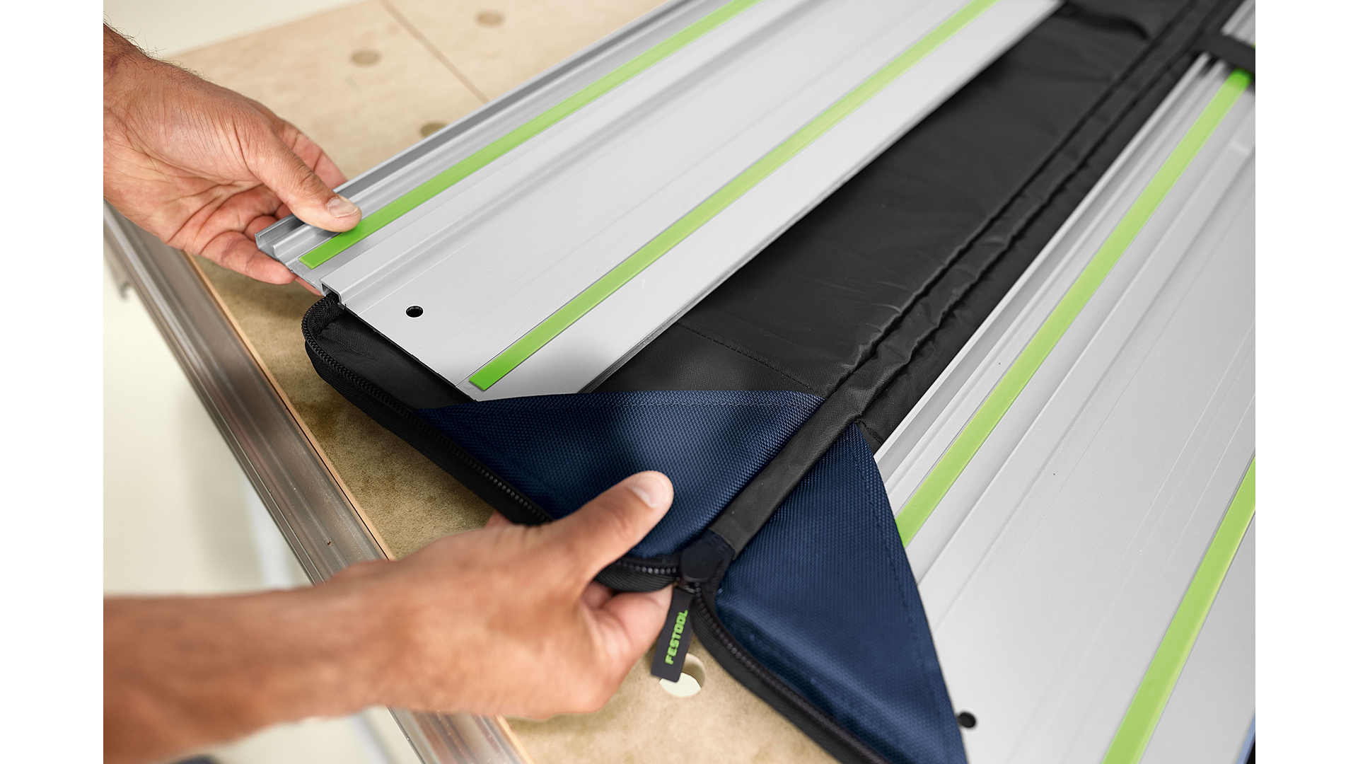 Hands placing aluminum guide rails with green stripes inside a protective soft carrying bag for woodworking tool accessories