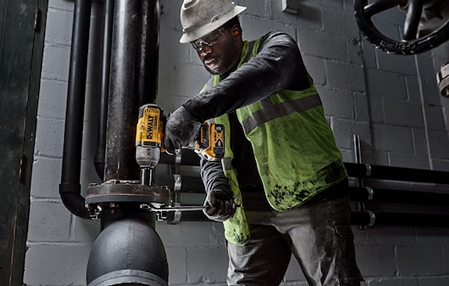 Worker using yellow and black 20V cordless high torque impact wrench on metal pipeline for home improvement tasks