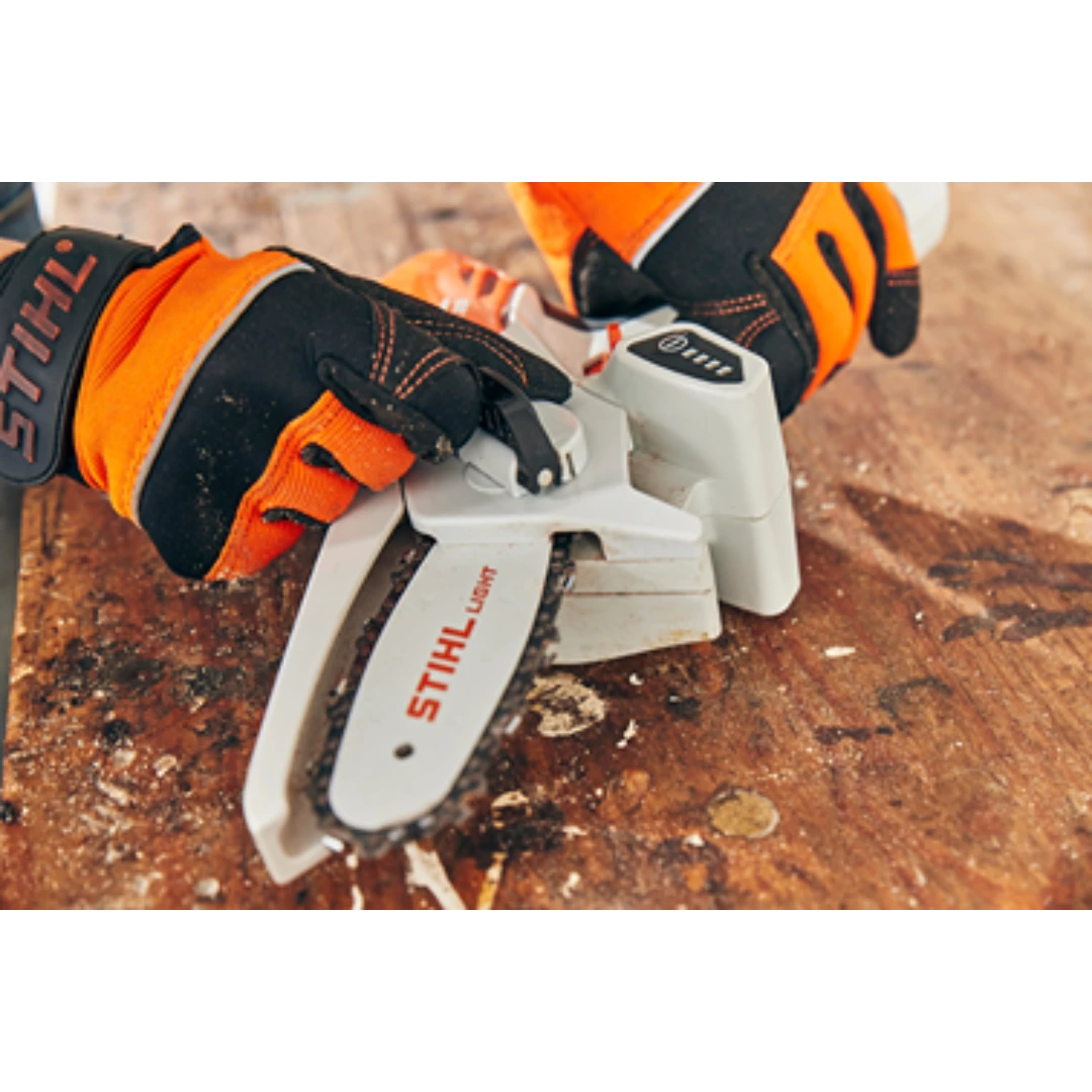 Hands wearing orange and black STIHL gloves adjusting a compact handheld battery garden pruner on a wooden surface