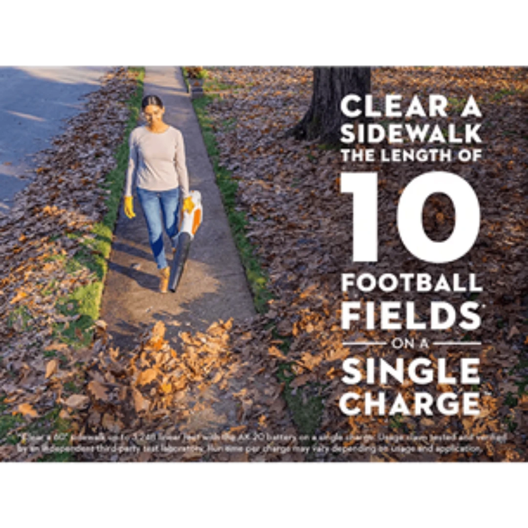 Person using an orange and white handheld blower clearing leaves from a sidewalk for home improvement tasks