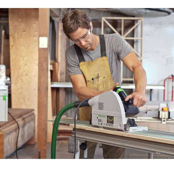 Worker using a Festool plunge cut saw with green dust extraction hose on wood panel in a workshop setting