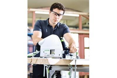Man wearing safety glasses using a Festool plungecut saw on wood in a power tools workshop environment