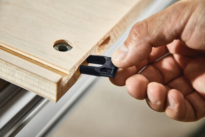 Hand inserting black plastic Festool corner connector into wooden panel groove for woodworking tool accessories and home improvement projects