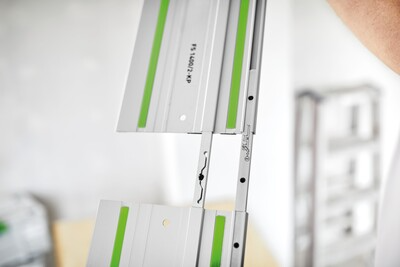 Close-up of a silver aluminum guide rail with green accents positioned vertically in a woodworking workshop setting