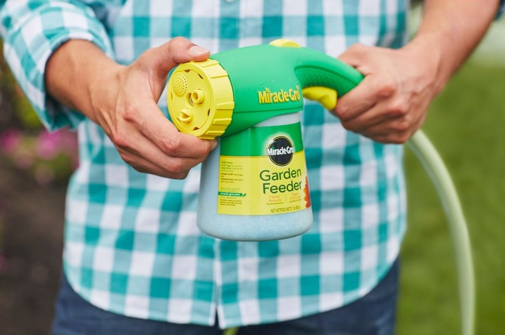 Green and yellow Miracle-Gro garden feeder held by person, designed for easy plant food application in lawn care tasks