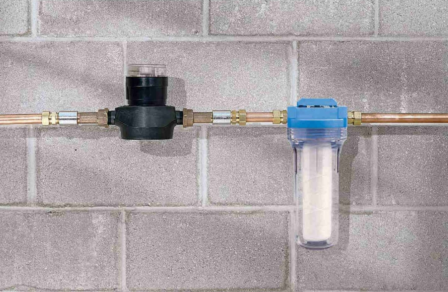 Blue-top water filter cartridge with transparent housing installed on copper piping against a concrete block wall