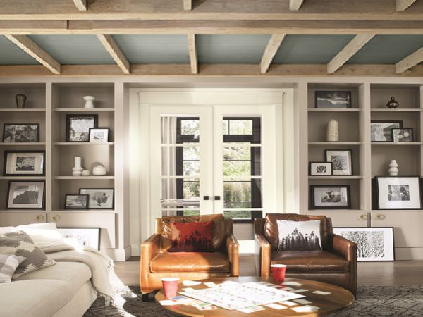 Cozy living room with leather armchairs, a round wooden coffee table, built-in shelves filled with framed photos and decorative items, and glass double doors letting in natural light.
