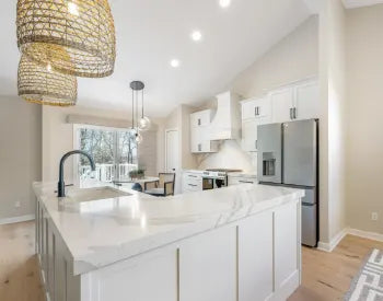 Bright contemporary kitchen with spacious white island, marble countertops, black faucet, pendant lighting, stainless steel refrigerator, and large windows.