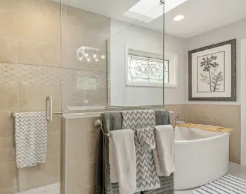 Elegant bathroom with a freestanding white bathtub, glass shower enclosure, chevron-patterned towels on a rack, and botanical wall art.