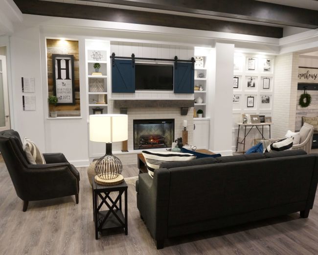 Cozy living room with dark upholstered sofas centered around a stone fireplace featuring blue sliding barn doors and built-in white shelving with decorative accents.