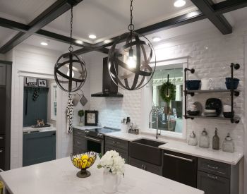 Cozy kitchen with white brick walls, dark cabinetry, large farmhouse sink, modern black range hood, and two spherical pendant lights over a white island.