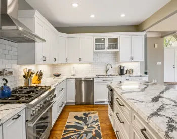 Bright traditional kitchen with white cabinetry, marble countertops, stainless steel appliances, subway tile backsplash, and hardwood floors.