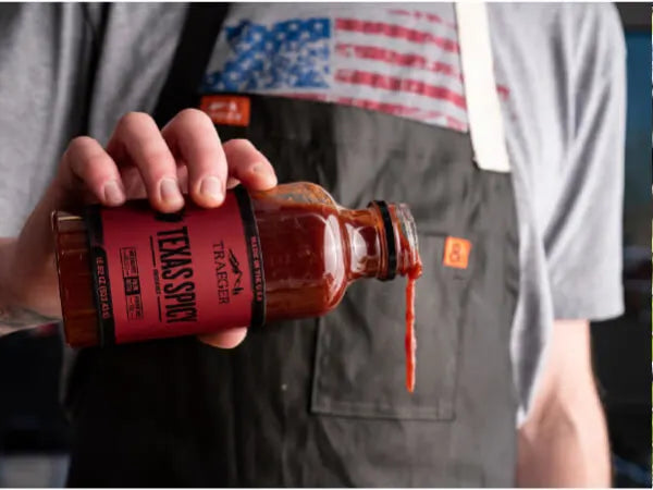 Person wearing an apron pouring thick barbecue sauce labeled Texas Spc from a glass bottle with a red label.