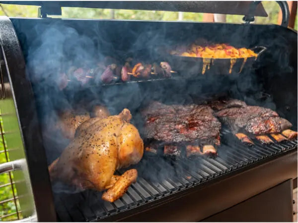 Open grill filled with smoky ribs and a whole seasoned chicken cooking over hot charcoal with visible smoke rising outdoors