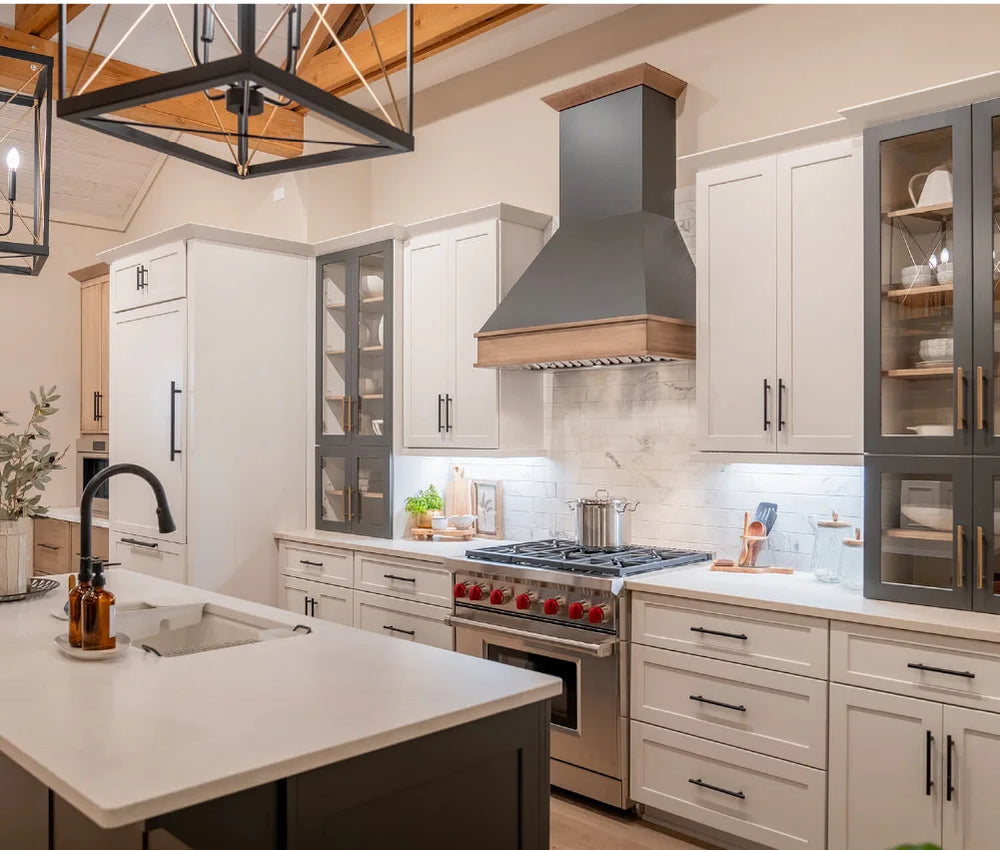 Bright kitchen with white cabinetry, contrasting dark hardware, glass display cabinets, stainless steel stove with wooden range hood, and a large island with a black faucet.