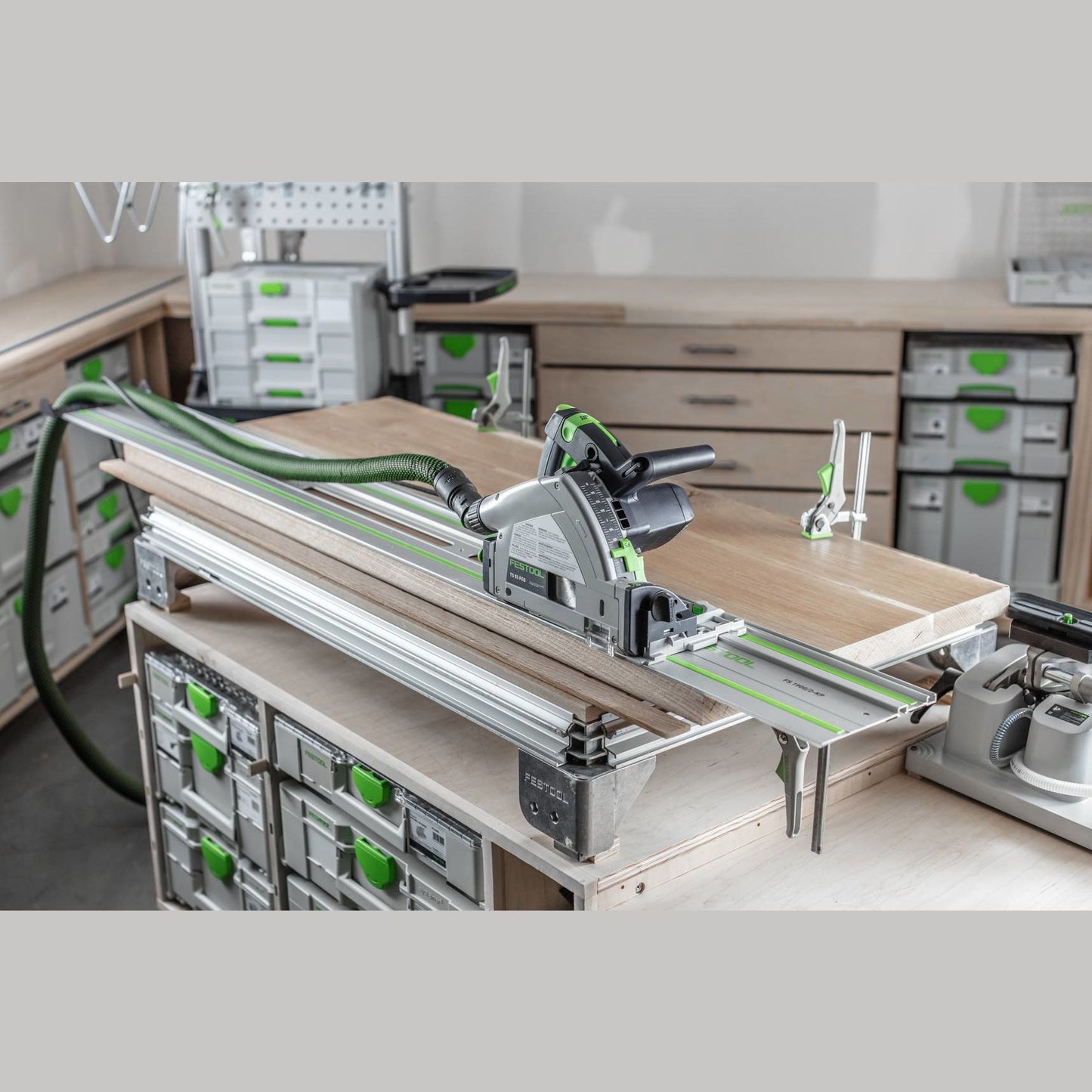 Festool plunge-cut track saw with guide rail and connected dust extraction hose in organized woodworking workshop