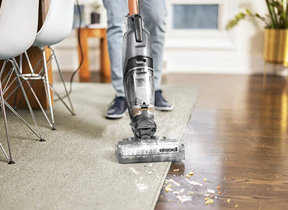 Multi-surface vacuum cleaner with water tank cleaning crumbs from carpet edge to hardwood floor in modern home interior