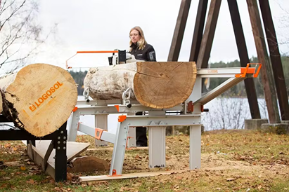 Person operating gray and orange portable chain sawmill with two log lifts for outdoor wood cutting tasks