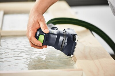 Person using a Festool sander with green button and dust extraction hose on wooden frame for home improvement