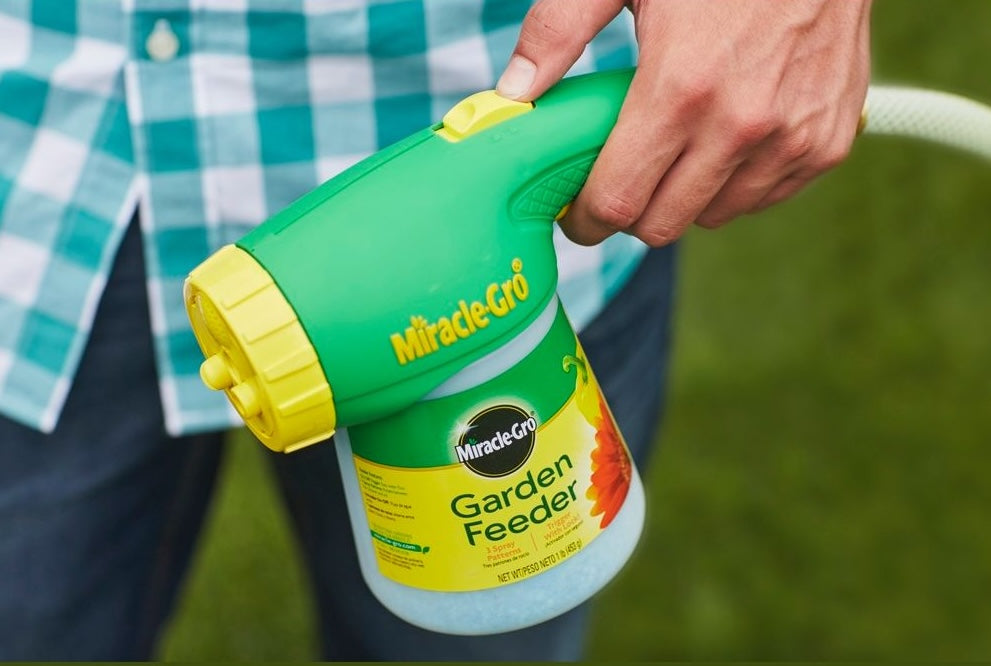 Handheld green and yellow garden feeder with trigger-lock for easy one-handed plant food application in lawn care tasks