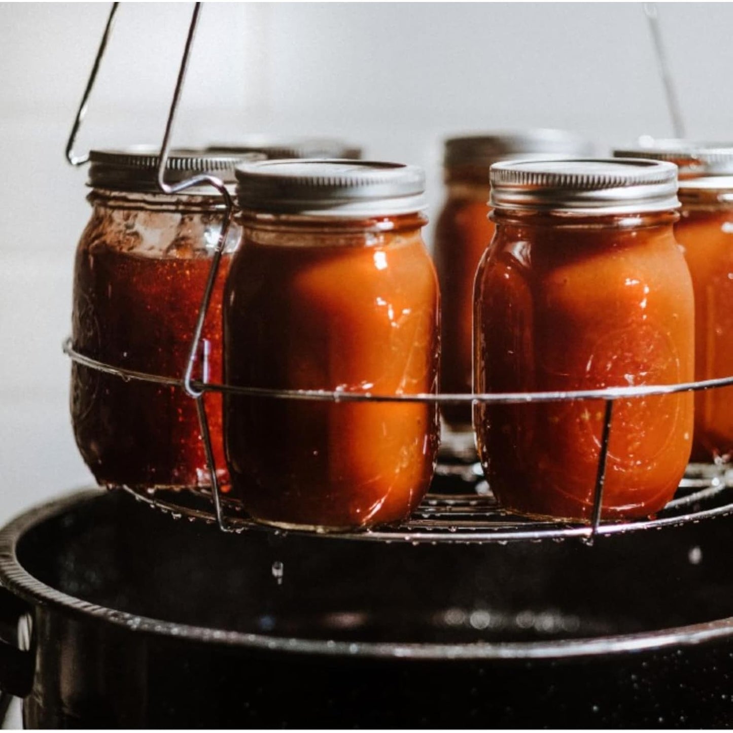Metal wire rack holding glass jars of preserved food inside a black speckled enamel steel canner pot for home use